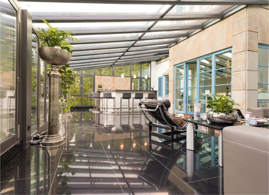 Architektonischer Kontrast und Harmonie durch einen modernen Wintergarten, der gezielt die Sandsteinelemente einer klassischen Fassade aufgreift.